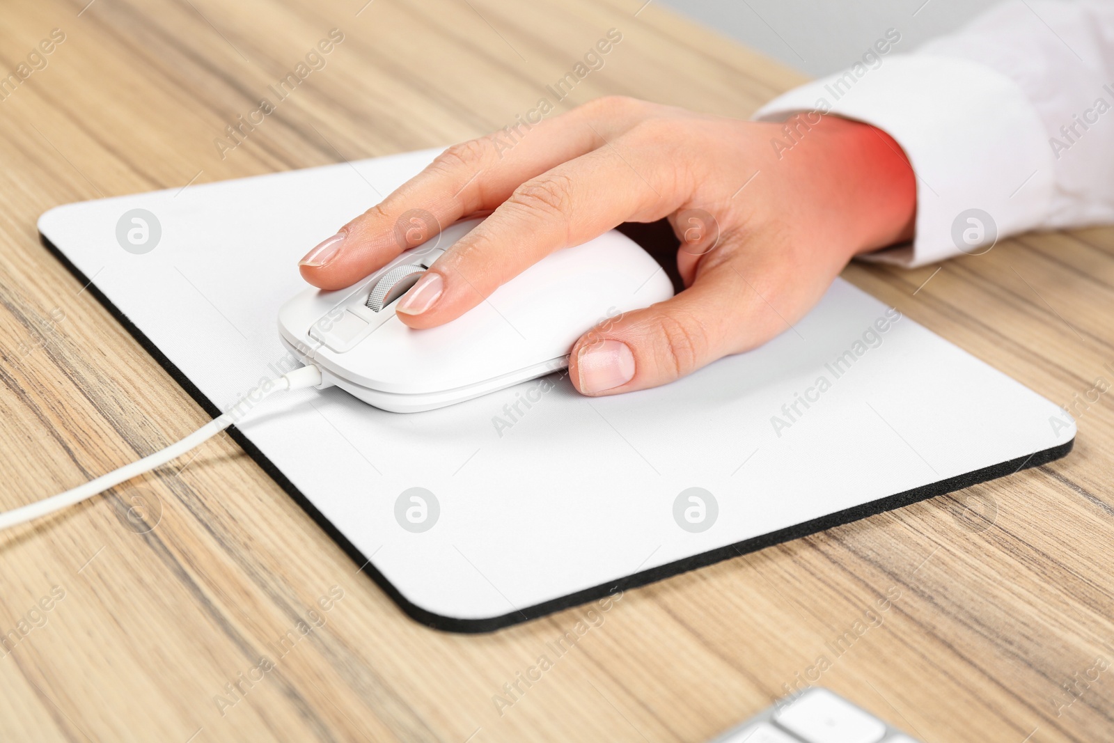 Image of Woman suffering from pain in wrist while using computer mouse at wooden table, closeup. Office work, Carpal tunnel syndrome