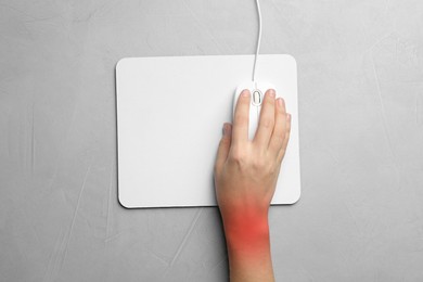 Image of Woman suffering from pain in wrist while using computer mouse at grey table, top view. Office work, Carpal tunnel syndrome