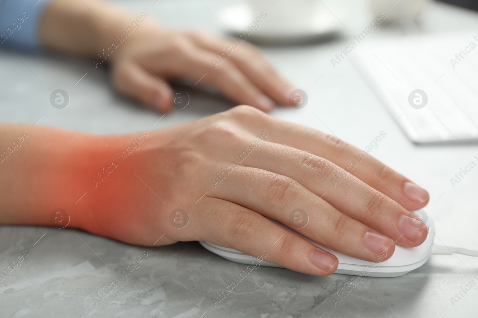 Image of Woman suffering from pain in wrist while using computer mouse at grey table, closeup. Office work, Carpal tunnel syndrome