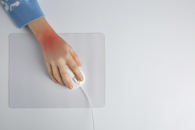 Image of Woman suffering from pain in wrist while using computer mouse at white table, top view. Office work, Carpal tunnel syndrome