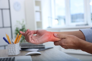 Image of Man suffering from pain in wrist at wooden table, closeup. Office work, Carpal tunnel syndrome