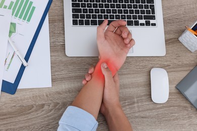 Image of Man suffering from pain in wrist at wooden table, top view. Office work, Carpal tunnel syndrome