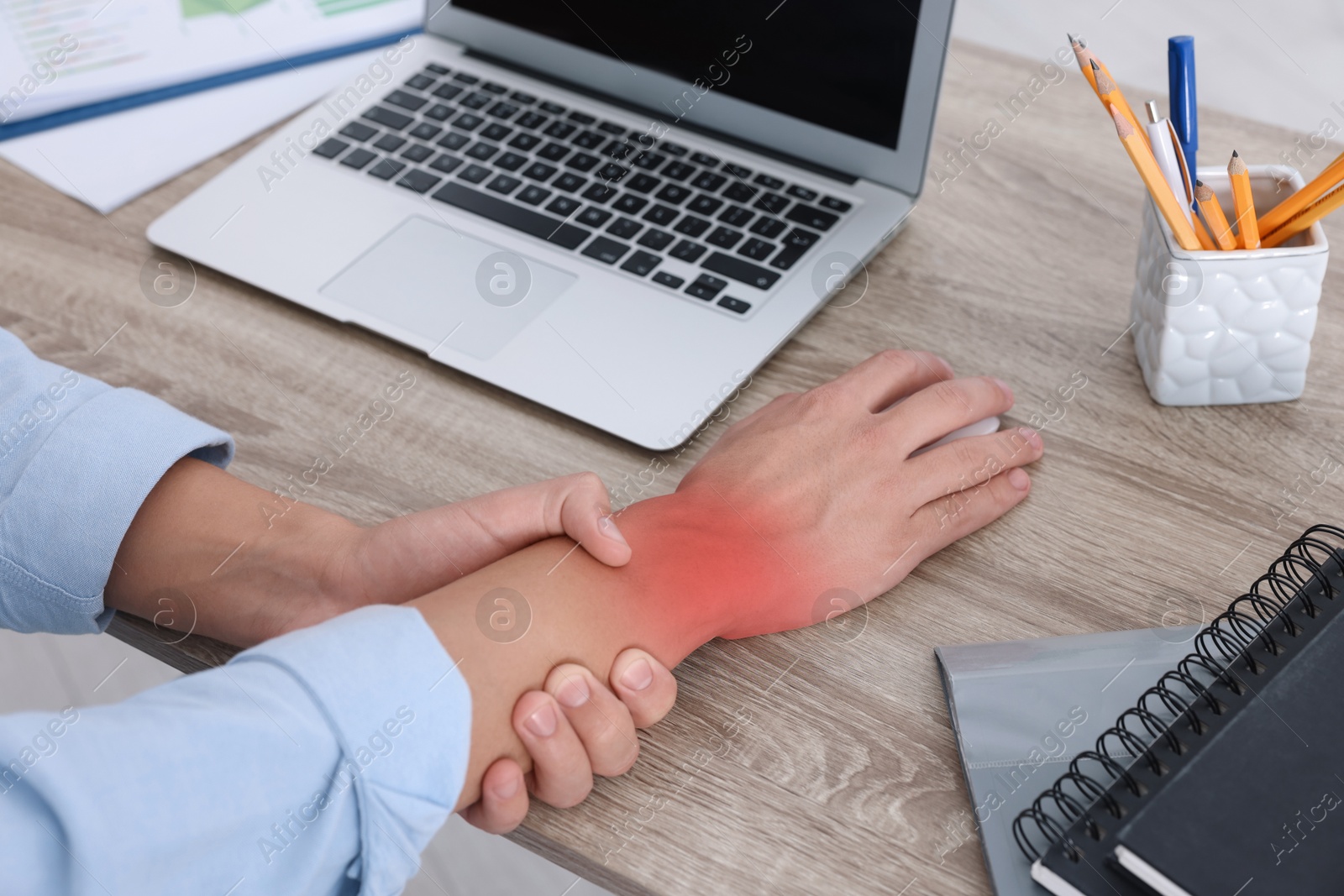 Image of Man suffering from pain in wrist while using computer mouse at wooden table, closeup. Office work, Carpal tunnel syndrome