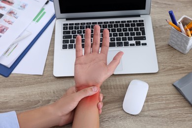 Image of Man suffering from pain in wrist at wooden table, closeup. Office work, Carpal tunnel syndrome