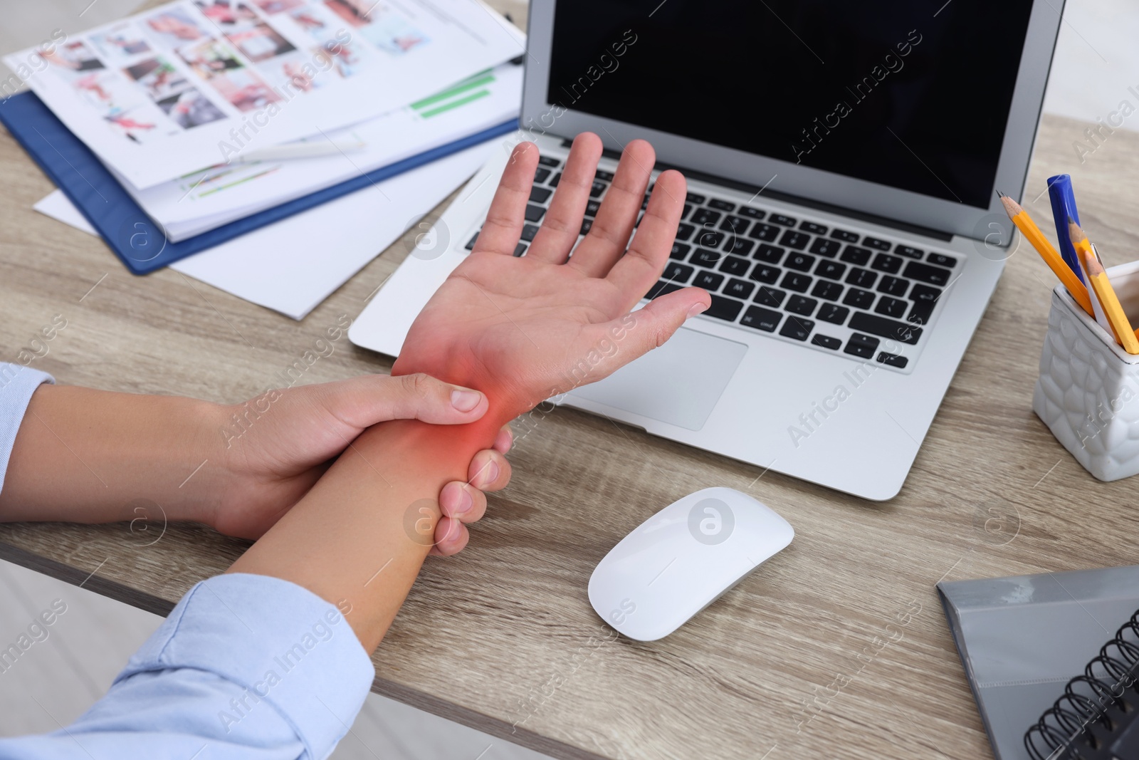 Image of Man suffering from pain in wrist at wooden table, closeup. Office work, Carpal tunnel syndrome