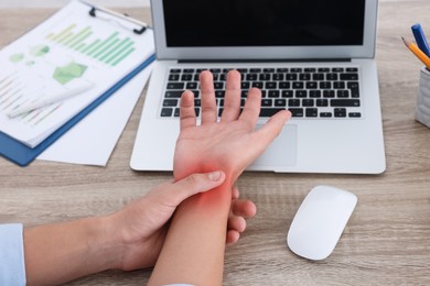 Image of Man suffering from pain in wrist at wooden table, closeup. Office work, Carpal tunnel syndrome