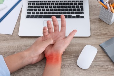 Image of Man suffering from pain in wrist at wooden table with laptop and computer mouse, closeup. Office work, Carpal tunnel syndrome