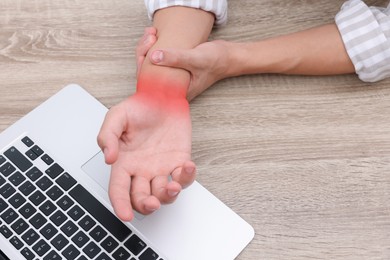 Image of Man suffering from pain in wrist at wooden table with laptop, closeup. Office work, Carpal tunnel syndrome