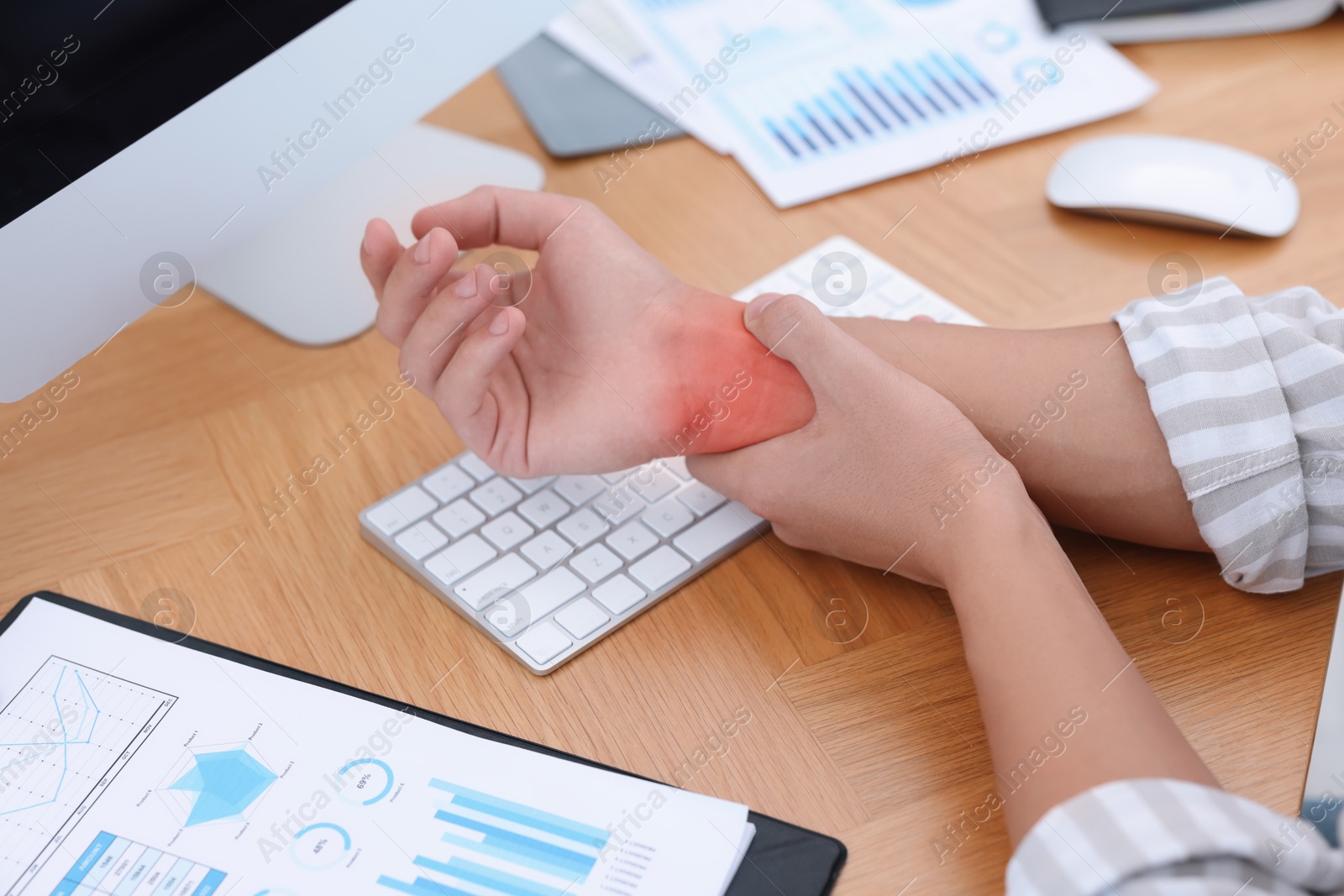 Image of Man suffering from pain in wrist at wooden table, closeup. Office work, Carpal tunnel syndrome