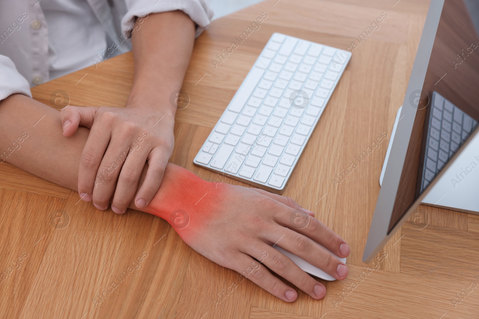 Image of Man suffering from pain in wrist while using computer mouse at wooden table, closeup. Office work, Carpal tunnel syndrome