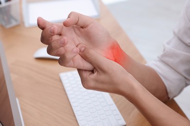 Image of Man suffering from pain in wrist at table, closeup. Office work, Carpal tunnel syndrome