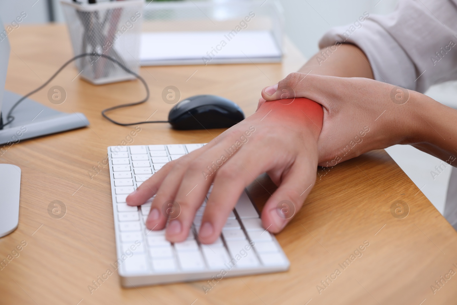 Image of Man suffering from pain in wrist at wooden table, closeup. Office work, Carpal tunnel syndrome