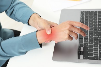 Image of Woman suffering from pain in wrist at white table with laptop, closeup. Office work, Carpal tunnel syndrome