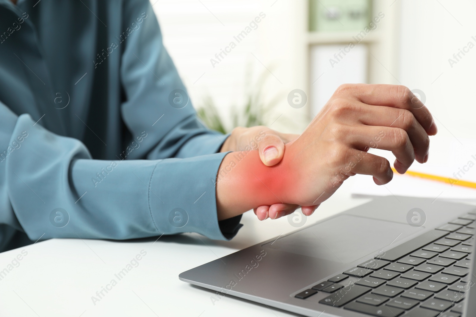 Image of Woman suffering from pain in wrist at white table with laptop, closeup. Office work, Carpal tunnel syndrome