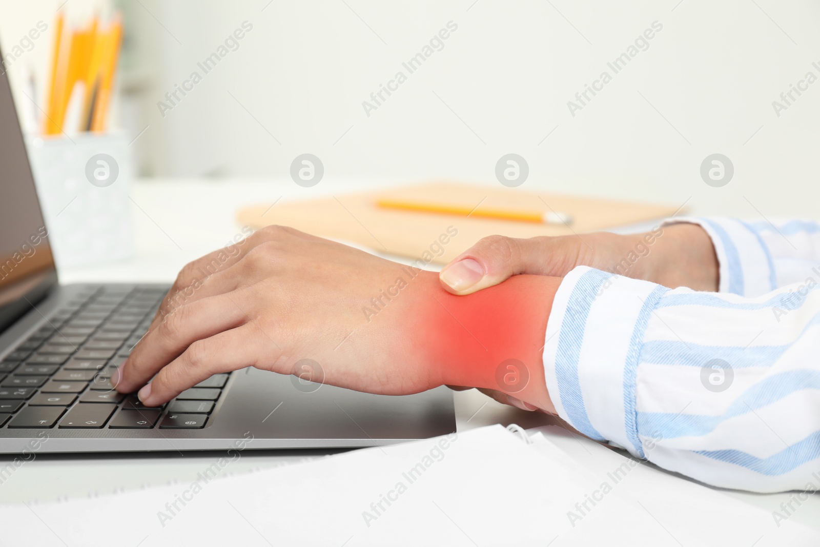 Image of Woman suffering from pain in wrist at table with laptop, closeup. Office work, Carpal tunnel syndrome