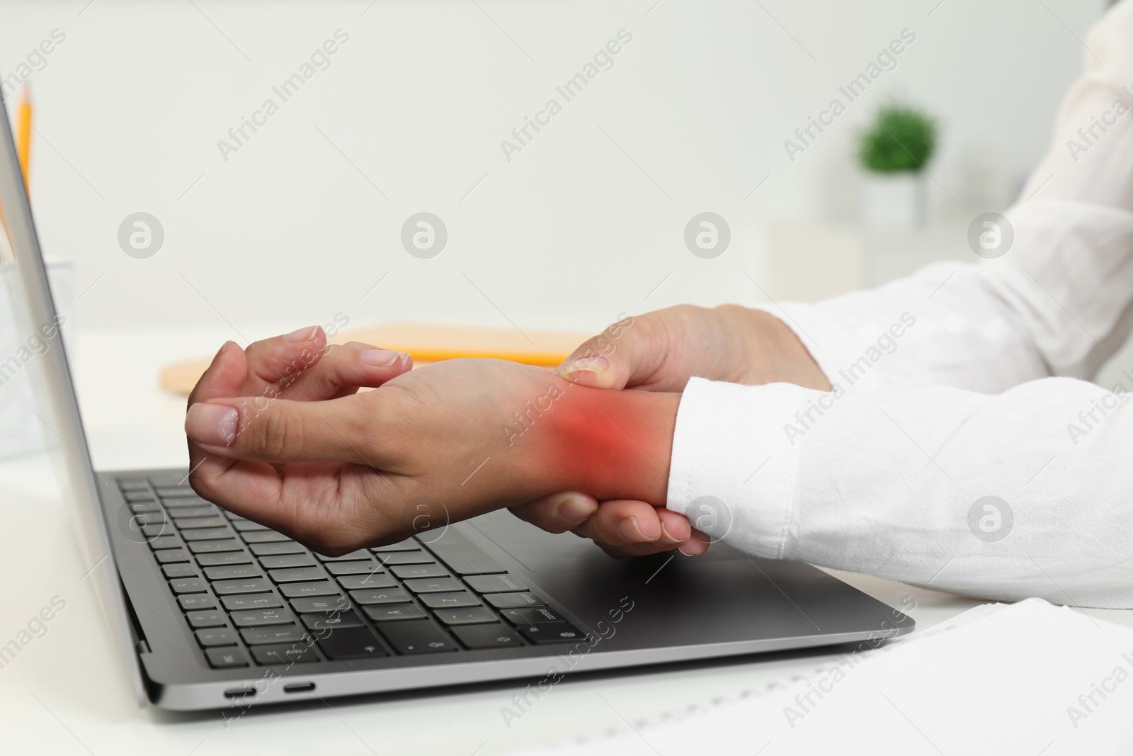 Image of Woman suffering from pain in wrist at white table with laptop, closeup. Office work, Carpal tunnel syndrome