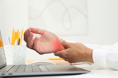 Image of Woman suffering from pain in wrist at white table with laptop, closeup. Office work, Carpal tunnel syndrome