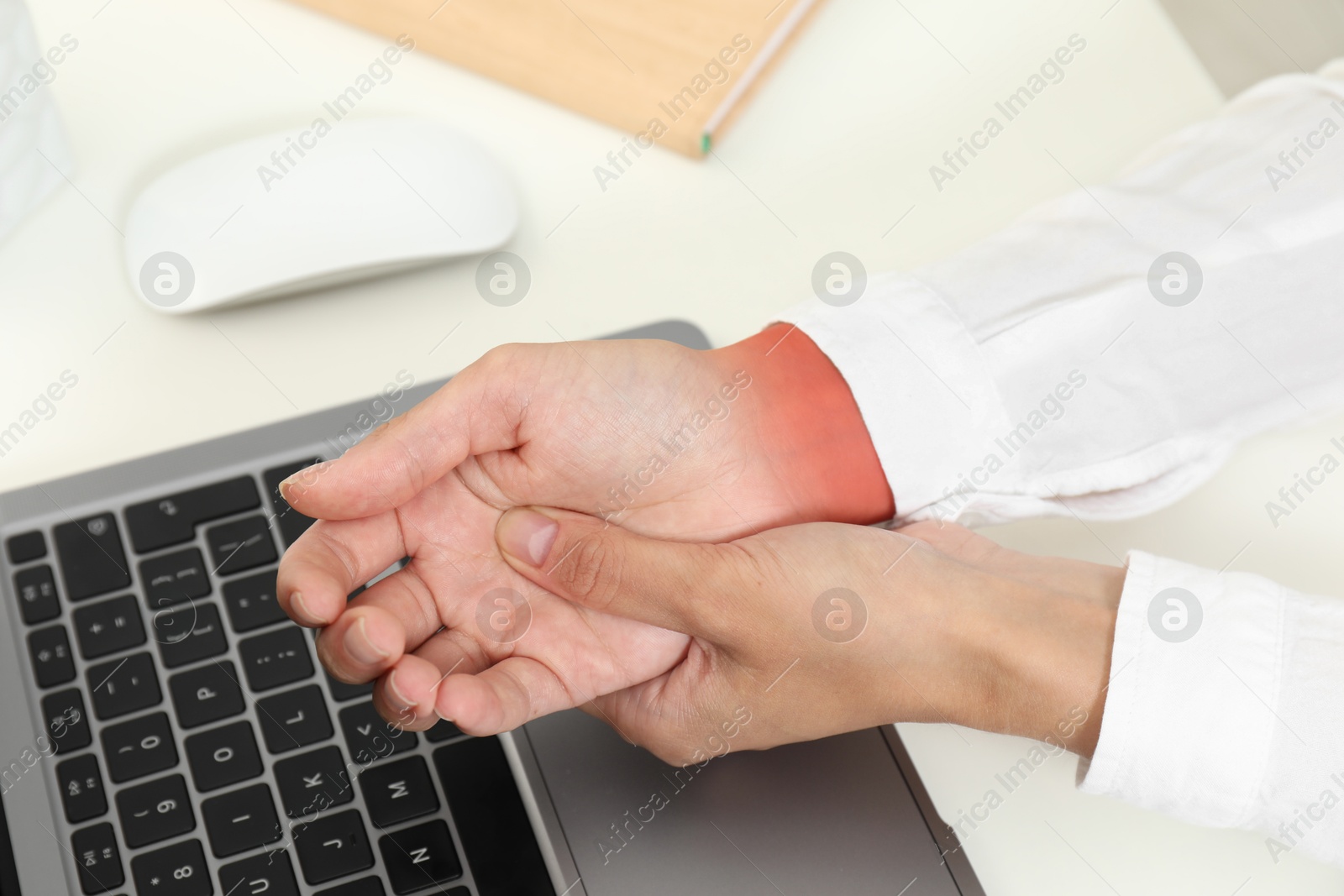 Image of Woman suffering from pain in wrist at white table with laptop, closeup. Office work, Carpal tunnel syndrome