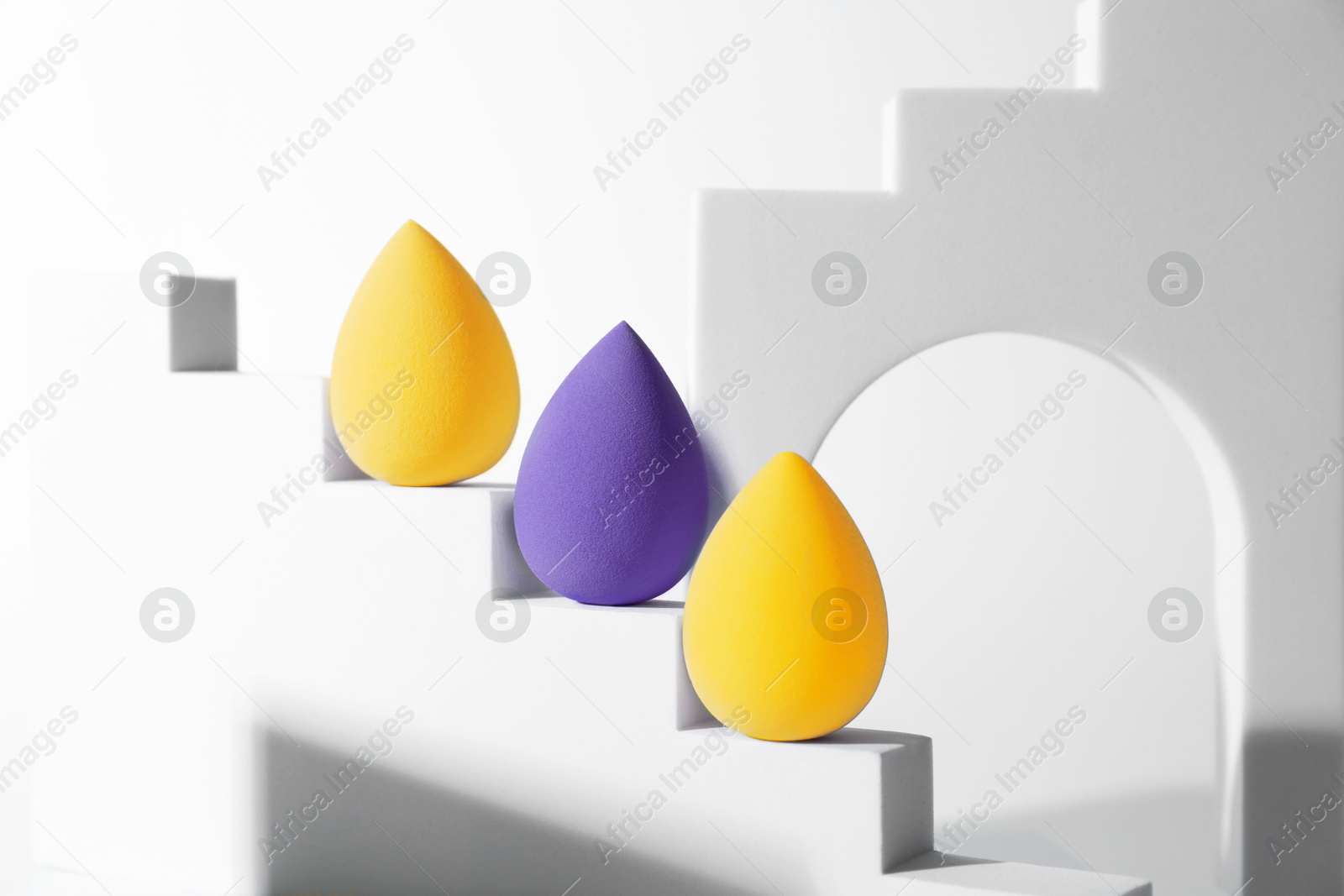 Image of Stylish presentation of blue violet and yellow makeup sponges on white background