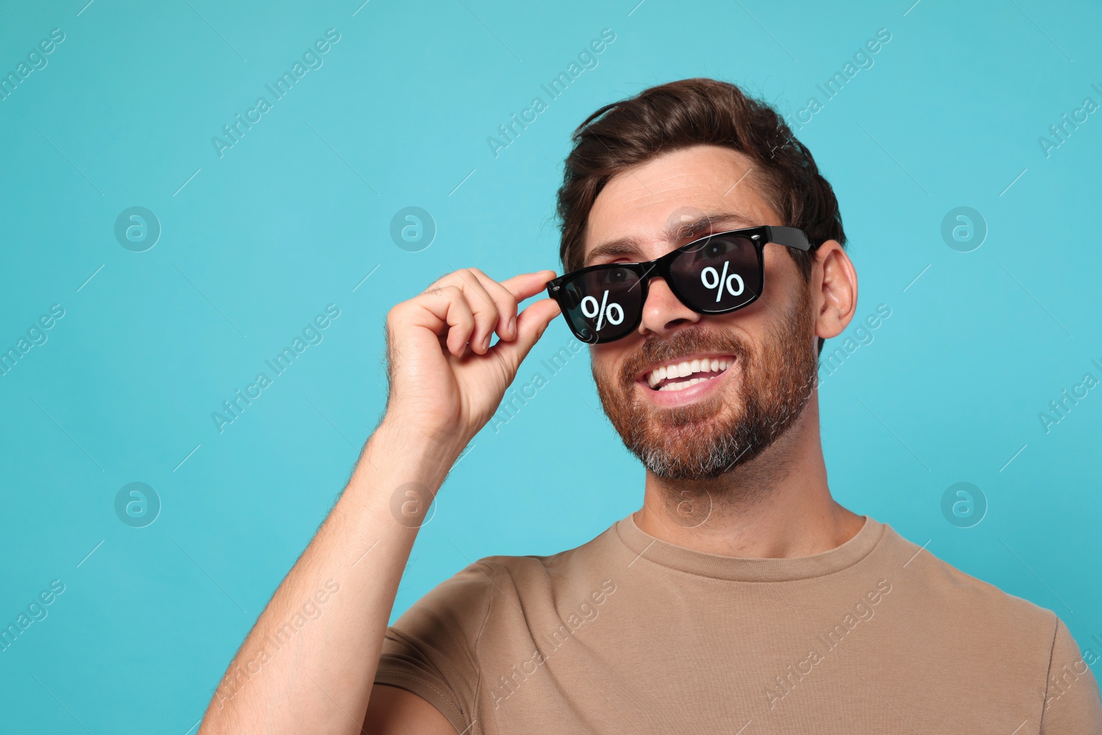 Image of Man with sunglasses smiling on turquoise background. Percent signs on lenses. Discount, hot offer