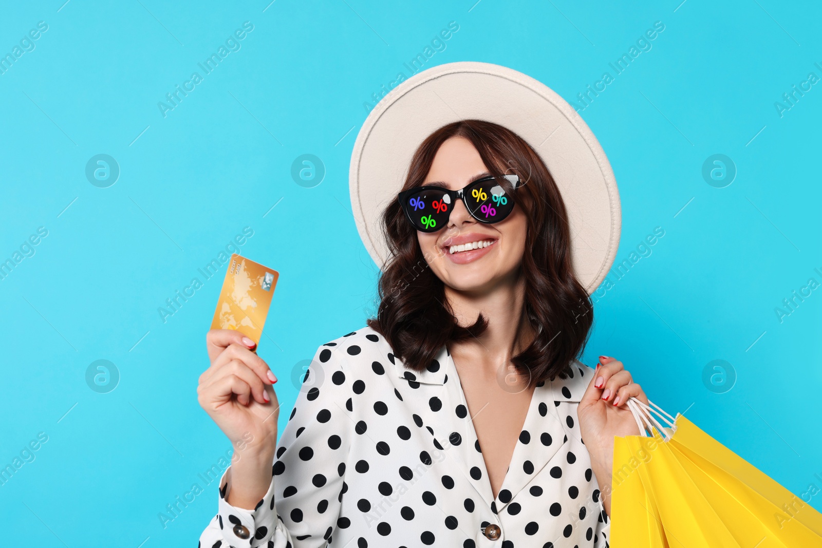 Image of Woman with sunglasses, credit card and shopping bags on light blue background. Percent signs on lenses. Discount, hot offer