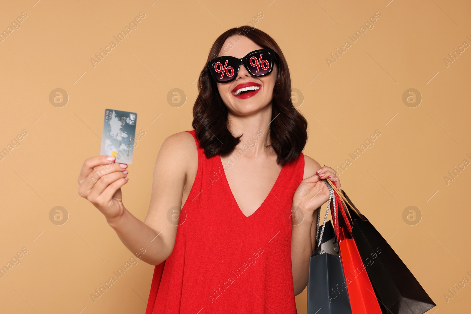 Image of Woman with sunglasses, credit card and shopping bags on dark beige background. Percent signs on lenses. Discount, hot offer