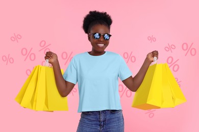 Woman with sunglasses and shopping bags on pink background. Percent signs on lenses. Discount, hot offer