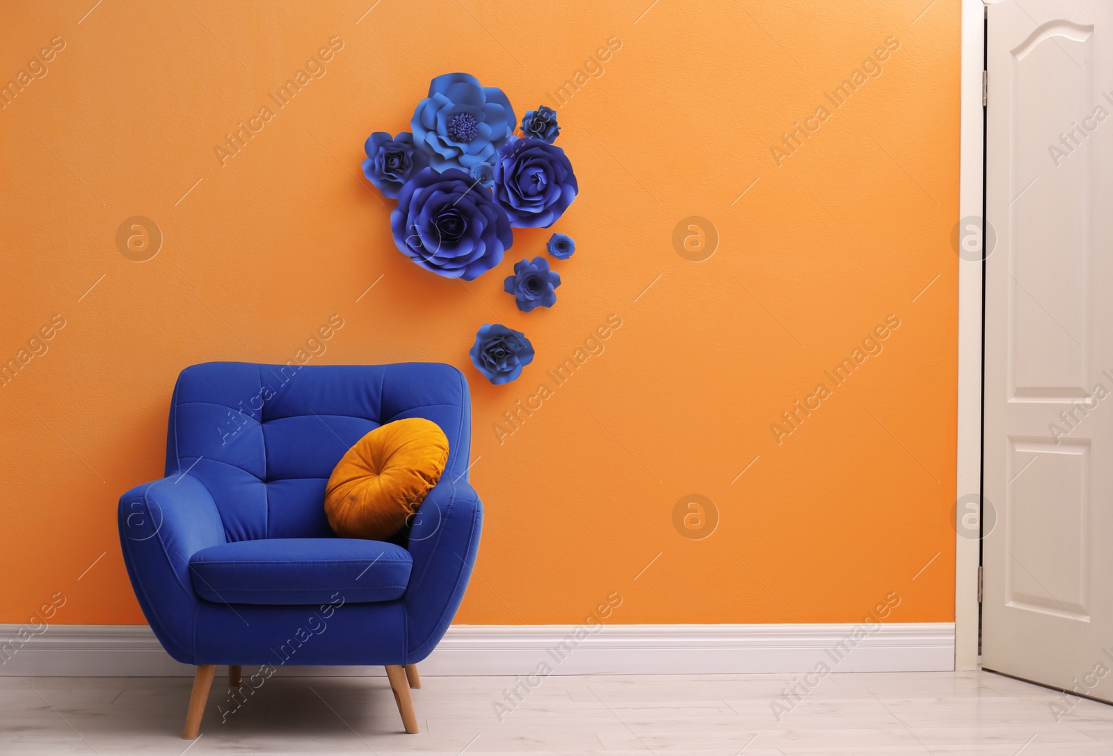 Image of Blue comfortable armchair near orange wall with floral decoration. Space for text