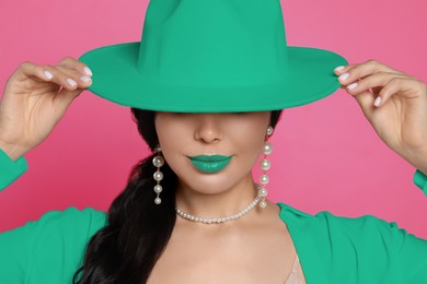 Fashionable woman with aquamarine color lipstick, hat and jacket on pink background