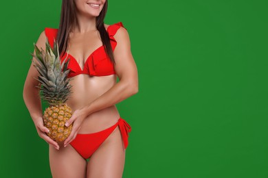 Image of Woman in red swimwear holding pineapple on green background. Space for text