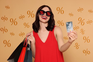 Image of Woman with sunglasses, credit card and shopping bags on dark beige background. Percent signs on lenses. Discount, hot offer