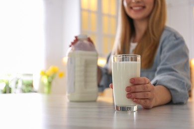 Photo of Young woman with gallon bottle of milk and glass at white marble table in kitchen, closeup. Space for text