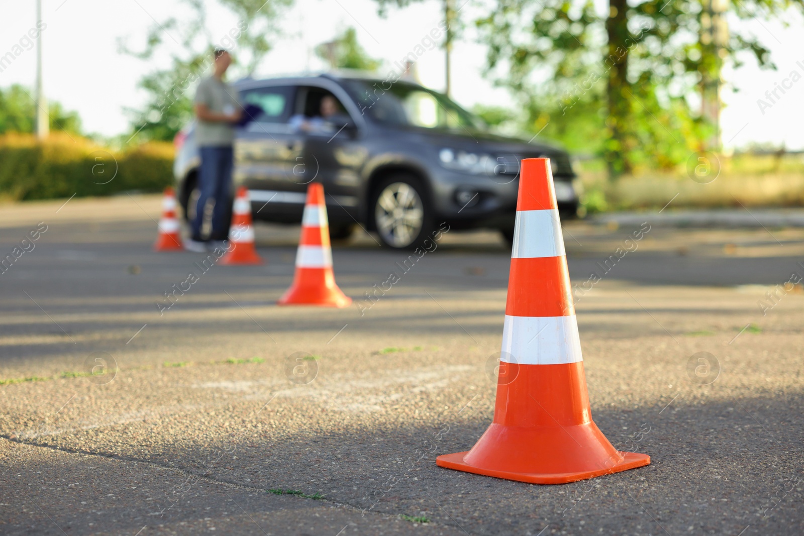 Photo of Examiner instructing student before exam at driving school test track, focus on traffic cone