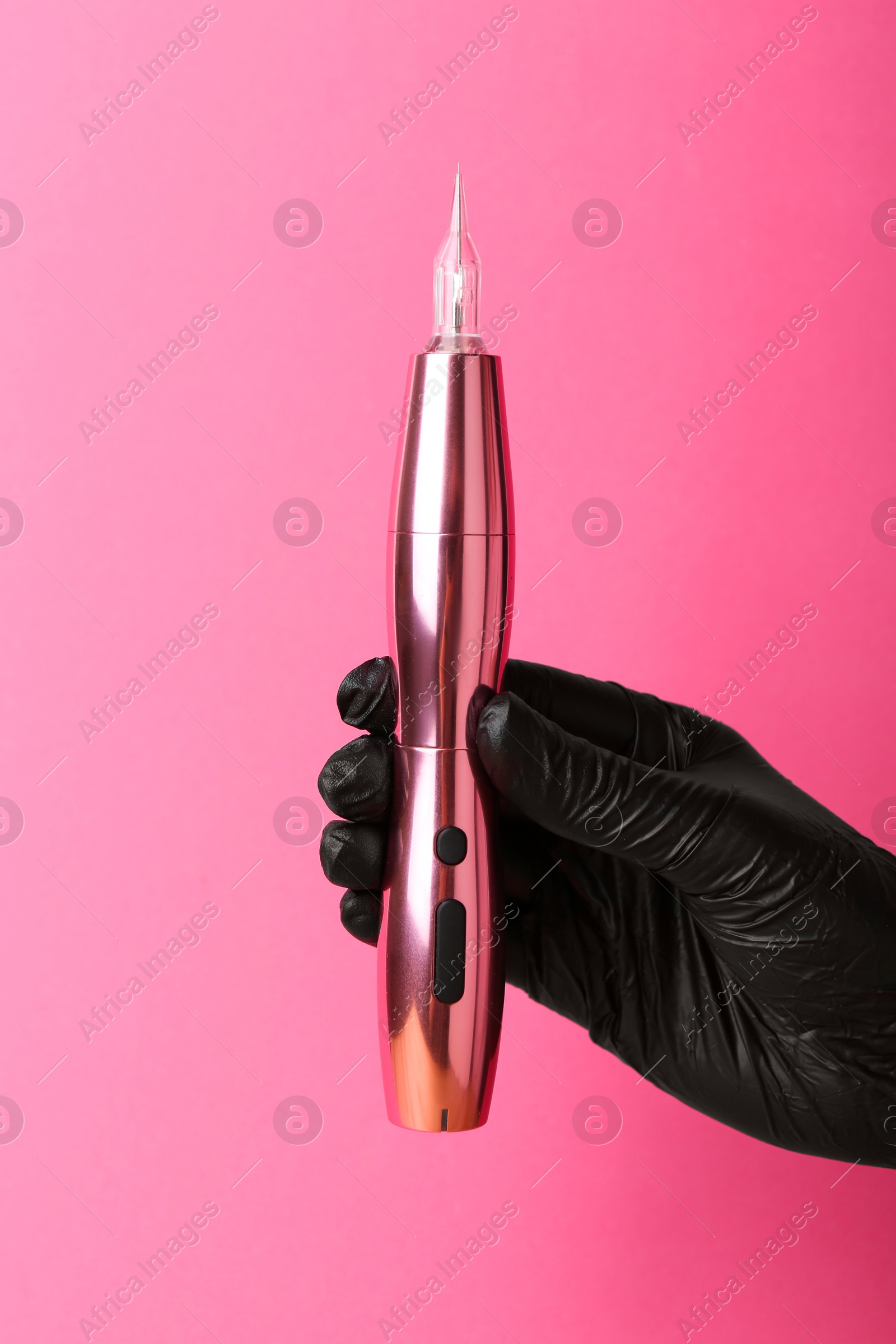 Photo of Professional cosmetologist holding permanent makeup machine on pink background, closeup