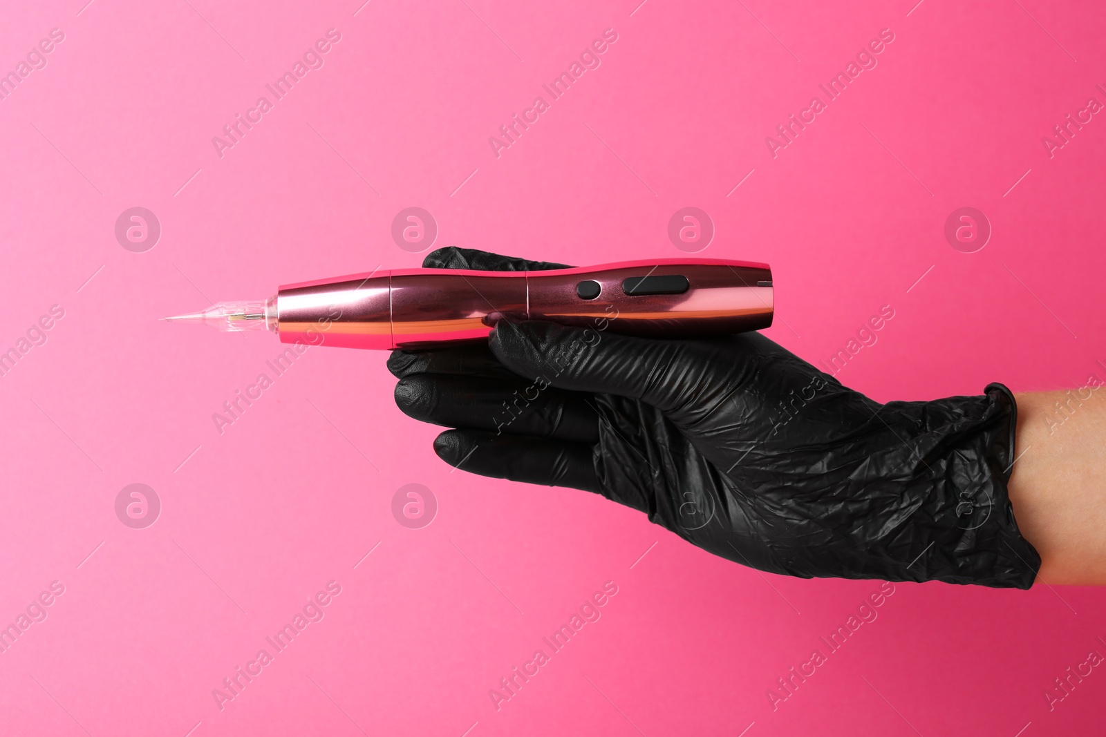 Photo of Professional cosmetologist holding permanent makeup machine on pink background, closeup