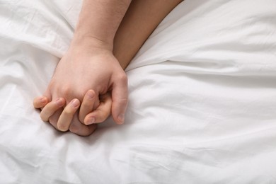 Photo of Lovely couple holding hands in bed, top view. Space for text