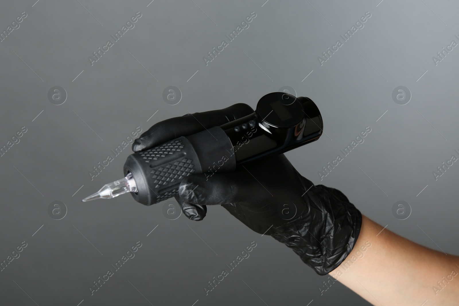 Photo of Professional cosmetologist holding permanent makeup machine on grey background, closeup