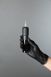 Photo of Professional cosmetologist holding permanent makeup machine on grey background, closeup