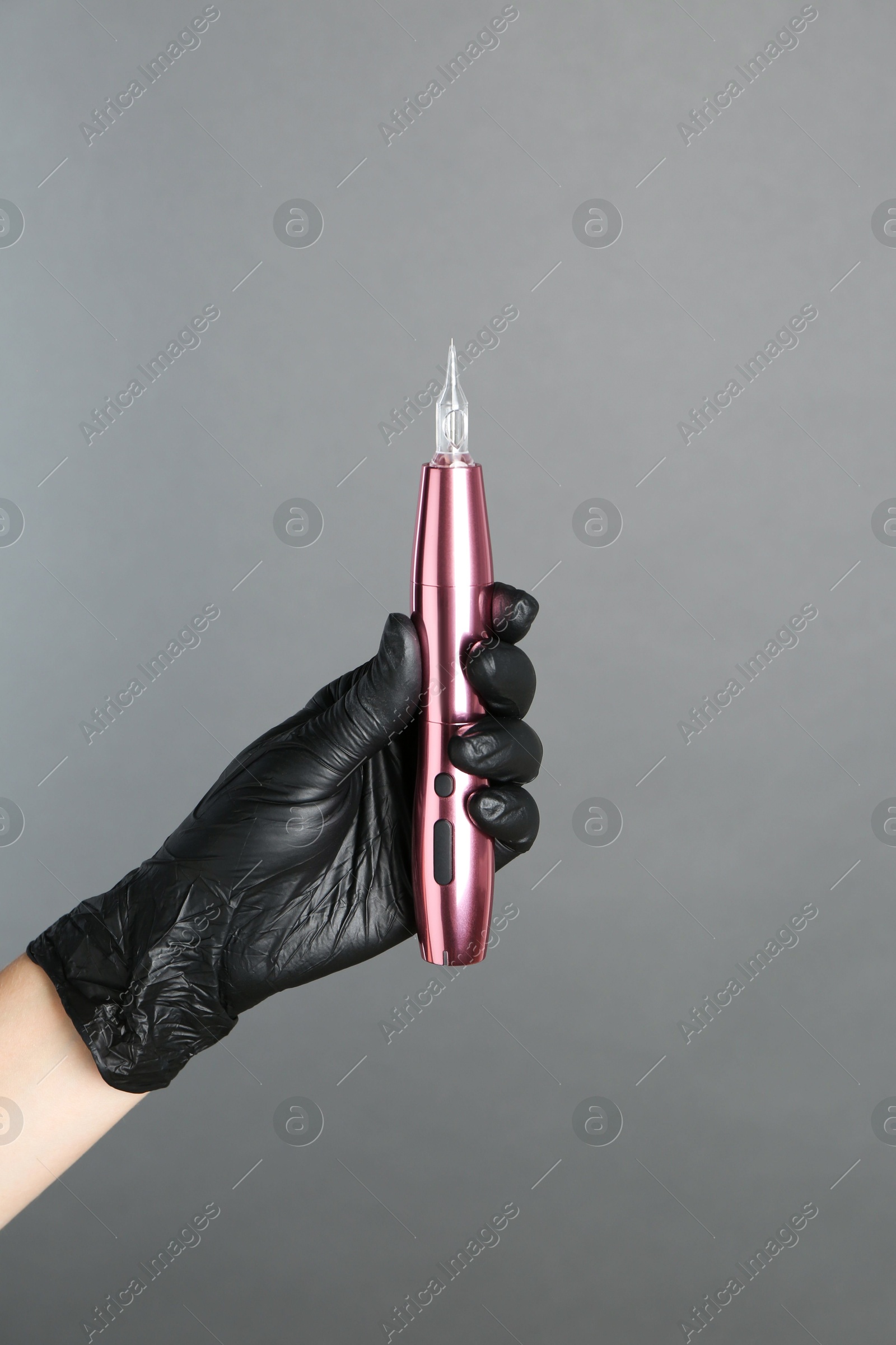 Photo of Professional cosmetologist holding permanent makeup machine on grey background, closeup