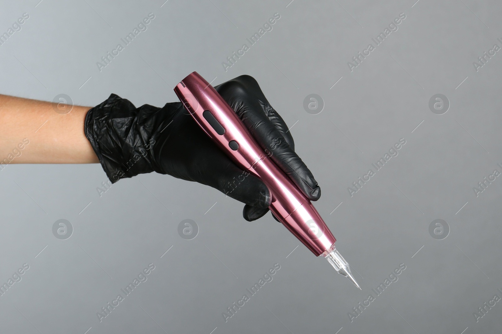 Photo of Professional cosmetologist holding permanent makeup machine on grey background, closeup