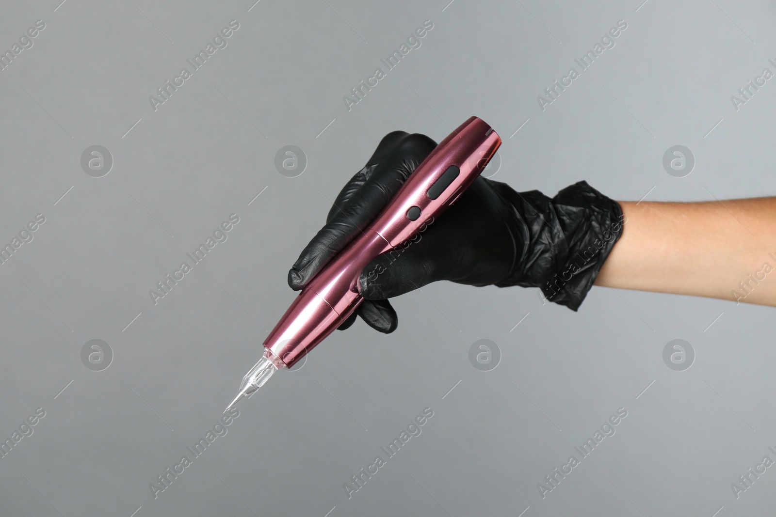 Photo of Professional cosmetologist holding permanent makeup machine on grey background, closeup