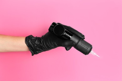 Photo of Professional cosmetologist holding permanent makeup machine on pink background, closeup