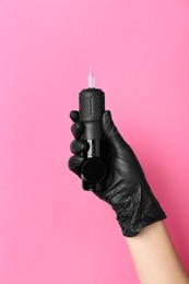 Photo of Professional cosmetologist holding permanent makeup machine on pink background, closeup