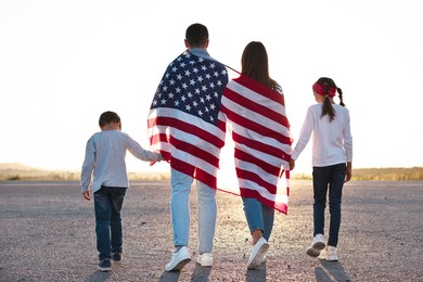 Family with flag of USA walking outdoors, back view