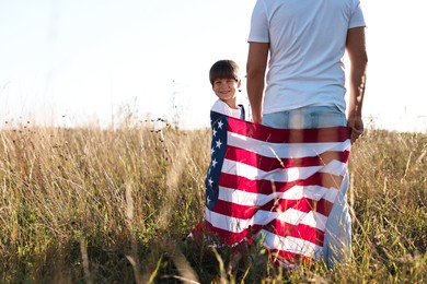 Father and son with flag of USA outdoors, back view. Space for text