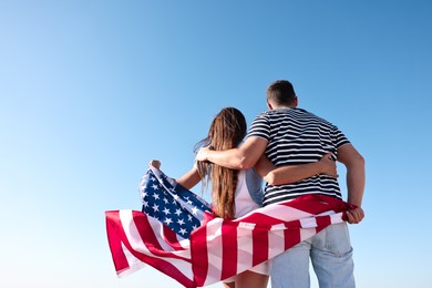 Photo of Couple with flag of USA outdoors, back view. Space for text