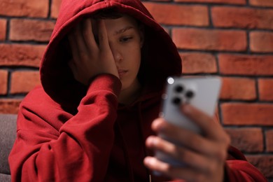 Loneliness concept. Sad teenage boy with smartphone near brick wall, selective focus