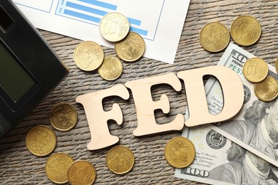 Photo of Letters Fed (Federal Reserve System), coins, dollar banknotes and calculator on wooden table, flat lay