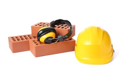 Red bricks, earmuffs and hard hat on white background