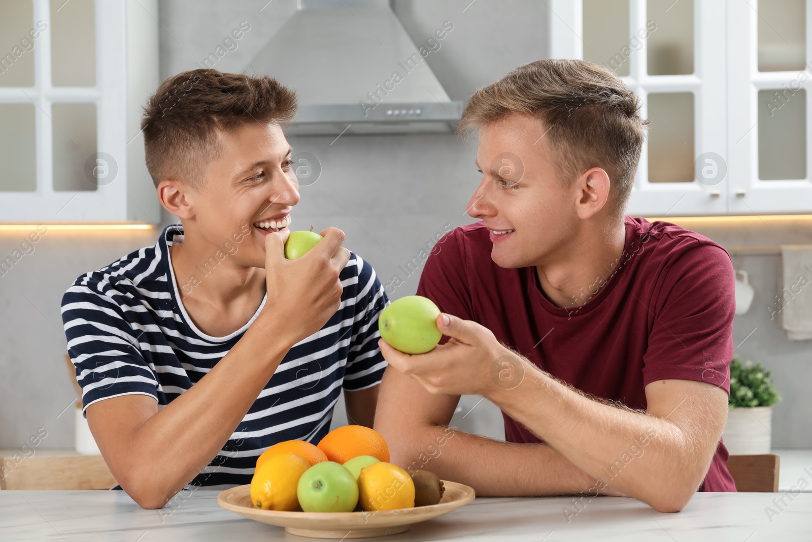 Photo of Happy brothers eating apples at table in kitchen